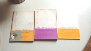 Foto de três documentos históricos em formato de livreto, com aspecto envelhecido, tarja colorida na parte de baixo, título “Infância Excepcional” no limite divisor das cores e número de publicação na lateral esquerda.