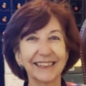 Foto da professora Maria Aparecida Lemes Reis sorridente. Ela é branca, tem olhos e cabelos castanhos, cabelos lisos e curtos e usa blusa de fundo azul com flores vermelhas.